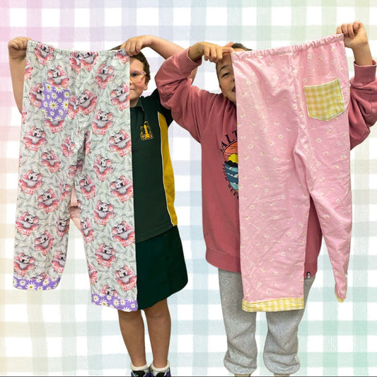 Two people holding up pairs of pajama pants against a checkered background