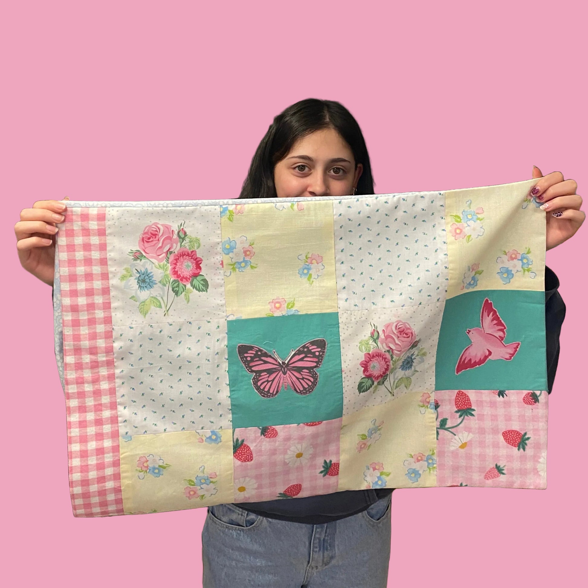 Person holding a colourful patchwork pillow case with butterfly designs.